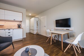A modern, well-lit living room with a dining area, a TV mounted on the wall, and a coat rack. - Haus Zingst, Appartement 23 für bis zu 4 Personen. - Haus Zingst (Fuhlendorf)