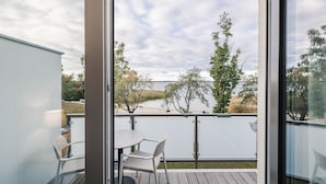 A balcony with a table and chairs, overlooking a lake with trees and a distant shoreline. - Haus Zingst, Appartement 24 für bis zu 4 Personen. - Haus Zingst (Fuhlendorf)