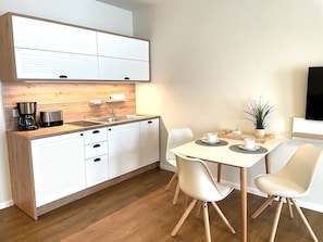 A modern kitchen with white cabinets, a wooden countertop, and a dining area with a white table and chairs.