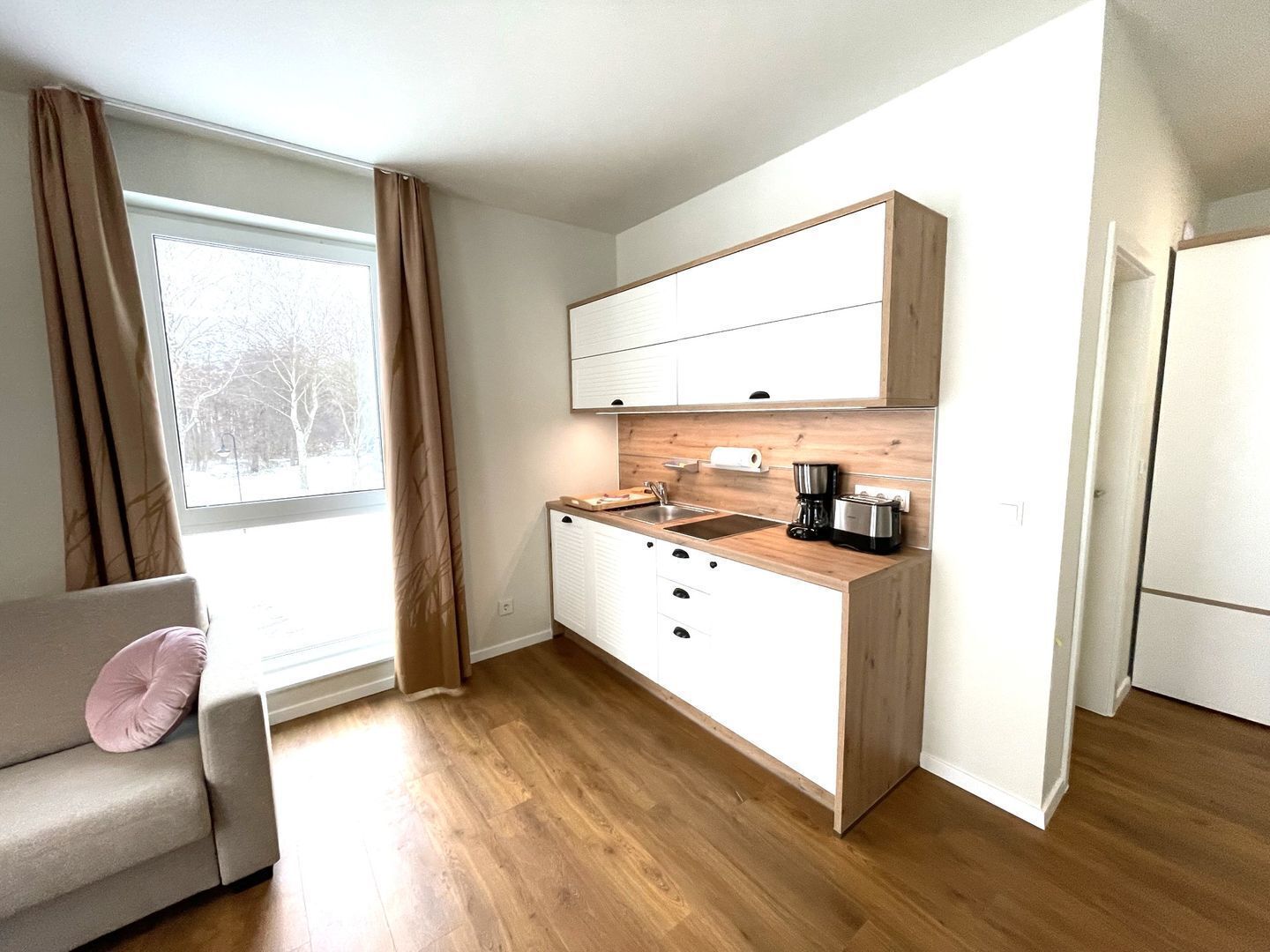 Une cuisine compacte dotée de plans de travail en bois, d’armoires blanches et d’un four encastré.