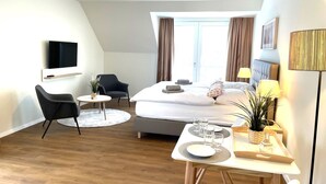A modern hotel room with a bed, two chairs, a small round table, a TV, and a window with curtains. - Haus Zingst, Appartement 28 für bis zu 2 Personen. - Haus Zingst (Fuhlendorf)
