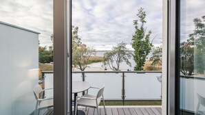 A balcony with a table and chairs, overlooking a lake with trees and a distant shoreline. - Haus Zingst, Appartement 31 für bis zu 2 Personen. - Haus Zingst (Fuhlendorf)