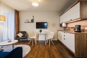 A modern, compact living space with a dining area, a sofa, a coffee table, a TV, and a kitchenette.