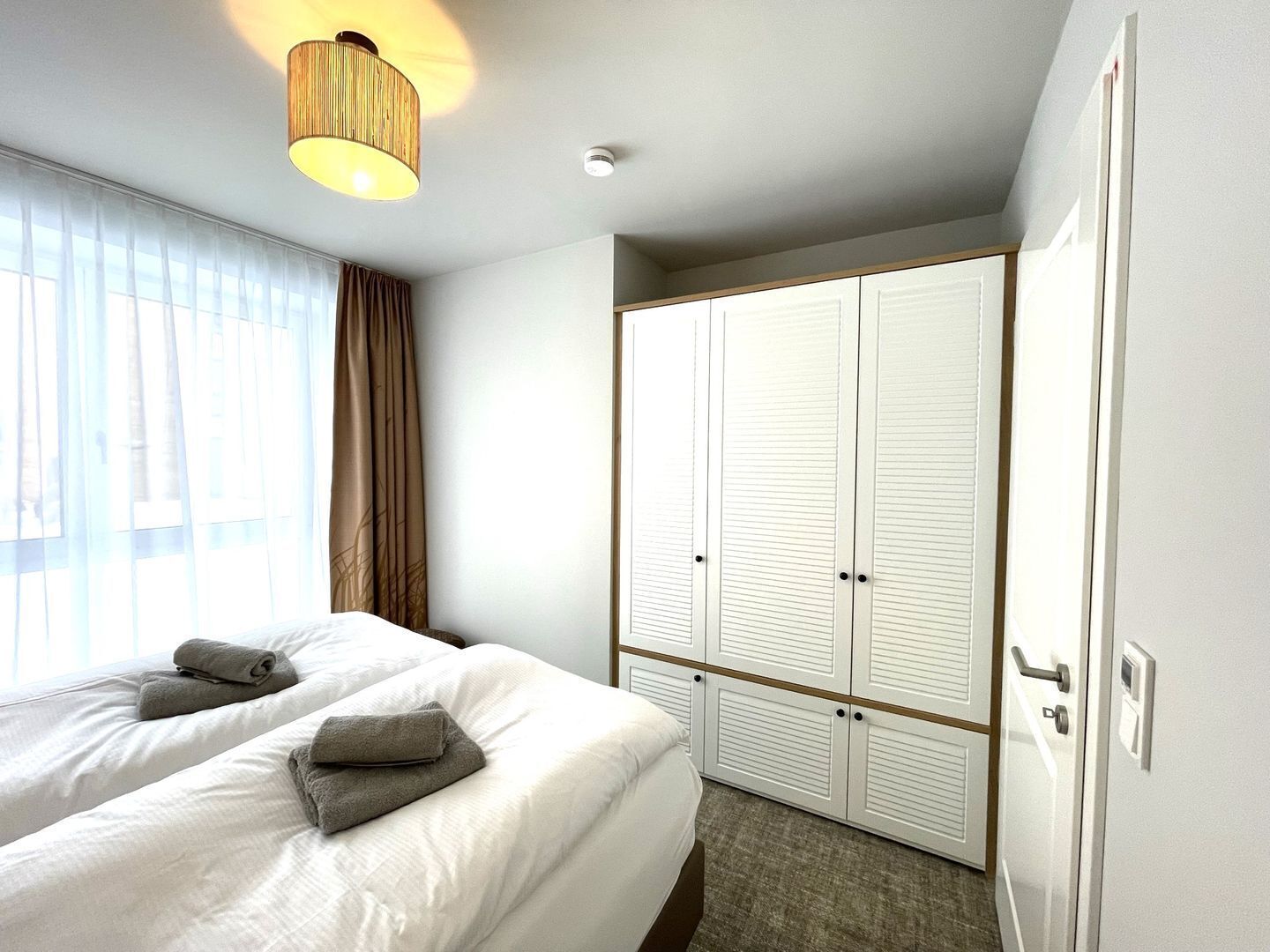 A hotel room with a bed, two pillows, a wardrobe, and a hanging light fixture.