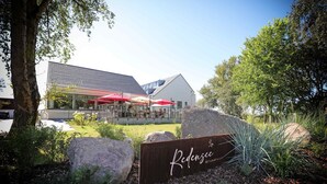 Un restaurant appelé « Redensee », doté d’une terrasse, d’un bâtiment moderne et d’un jardin aménagé.