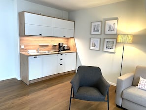 Una cocina moderna con armarios blancos y encimera de madera, un sillón gris y un sofá gris con un cojín estampado.