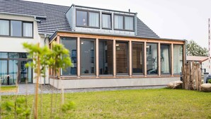 Una casa moderna con ventanas amplias, techo inclinado y césped cuidado.