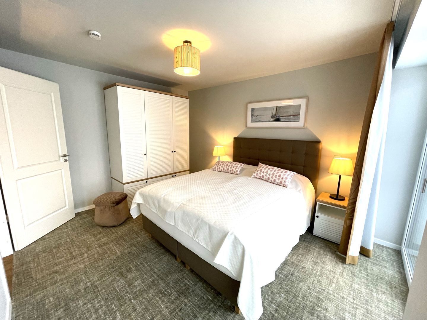 Une chambre à coucher avec un grand lit, deux lampes de chevet, une armoire et un petit tabouret.