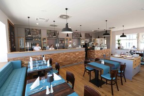 Un restaurant avec un plancher en bois, des sièges rembourrés en tissu bleu et un comptoir où travaille un barista.