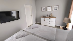 Ein Hotelzimmer mit zwei Betten, einer weißen Kommode, einem Flachbildfernseher und gerahmten Bildern an der Wand.