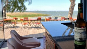 A bar area with a bottle of Störtebeker beer, a view of the beach, and outdoor seating.