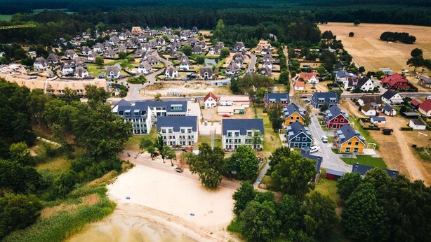 An aerial view of a residential area with houses, a sandy beach, and a water body.