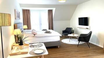 Une chambre d’hôtel moderne équipée d’un lit, d’une table de chevet, d’une lampe, d’une chaise, d’un téléviseur et d’un petit coin repas.