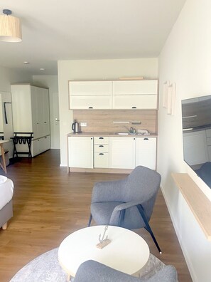 A modern living room with a grey armchair, a small white table, and a TV mounted on the wall. - Haus Prerow, Appartement 37 für bis zu 2 Personen. - Haus Prerow (Fuhlendorf)