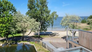 Una terraza de madera con vista a una playa, un cuerpo de agua tranquilo, árboles y un cielo despejado.