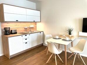 A modern kitchen with white cabinets, a wooden countertop, and a dining area with a white table and chairs. - Haus Prerow, Appartement 41 für bis zu 2 Personen. - Haus Prerow (Fuhlendorf)