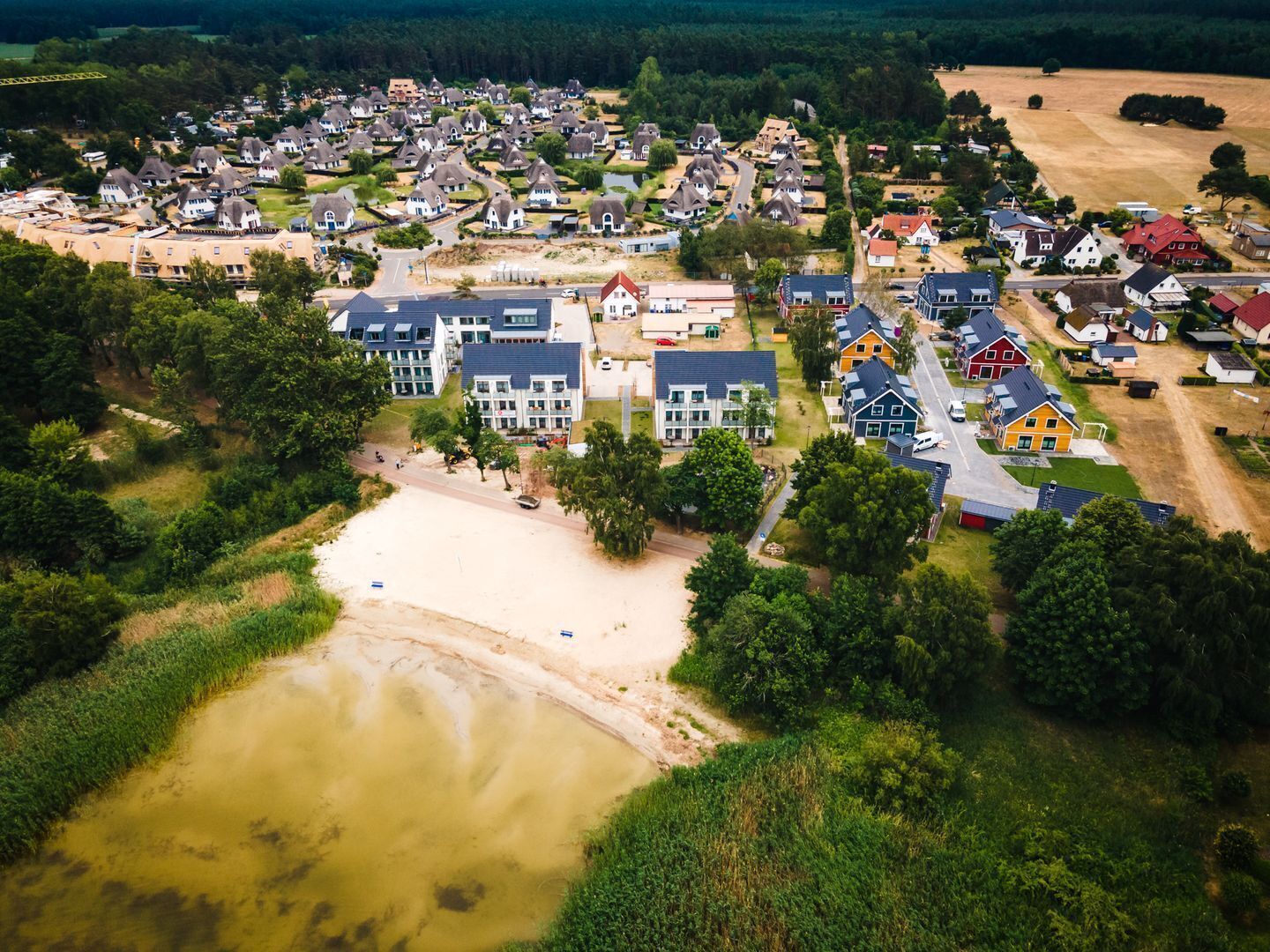 An aerial view of a residential area with houses, a sandy beach, and a water body.
