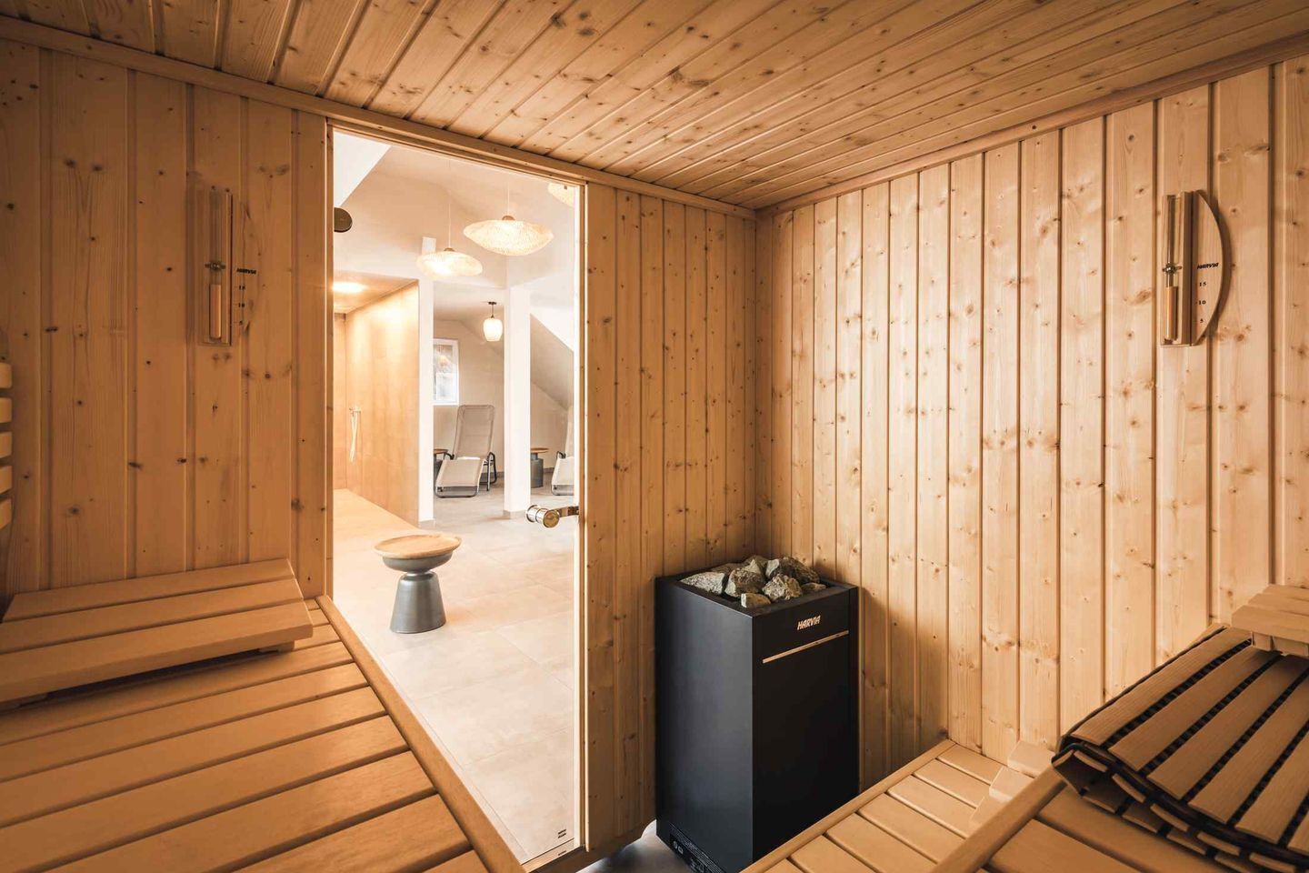 A sauna room with wooden walls, a bench, a sauna heater, and a toilet.