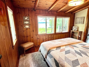 A wooden cabin bedroom with a bed, a bench, a window, and a fan. - Lakeside Log Cabin - Enjoy a beautiful sugar sand beach, Fireplace (Augusta)