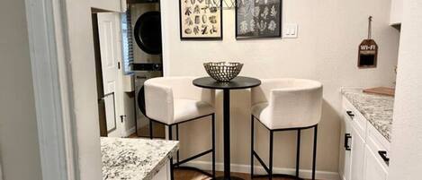 A compact kitchen with two white bar stools, a round table, and a hanging light fixture.