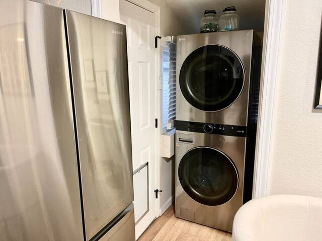 A compact kitchen with a stainless steel refrigerator and a stacked washer and dryer.