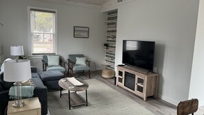 Una sala de estar moderna con una televisión de pantalla plana, dos sillones, un sofá, una mesa de centro y una lámpara.