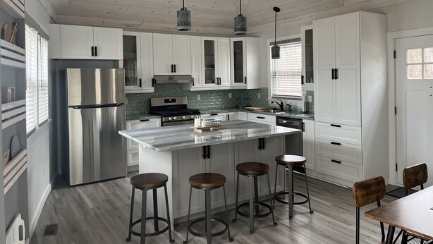 Una cocina moderna con armarios blancos, un refrigerador de acero inoxidable, una isla de mármol con taburetes e iluminación colgante.