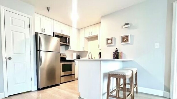 Una cocina moderna con electrodomésticos de acero inoxidable, piso de madera e isla blanca con taburetes de bar.