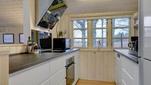 A modern kitchen with wooden walls, a built-in oven, a coffee maker, and a window with a view of trees. - Charming holiday home close to water (Sæby)
