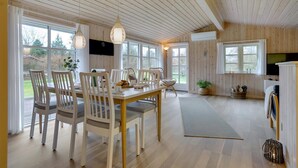 A spacious room with a wooden ceiling, large windows, a dining table with chairs, a sofa, and a TV. - Charming holiday home close to water (Sæby)