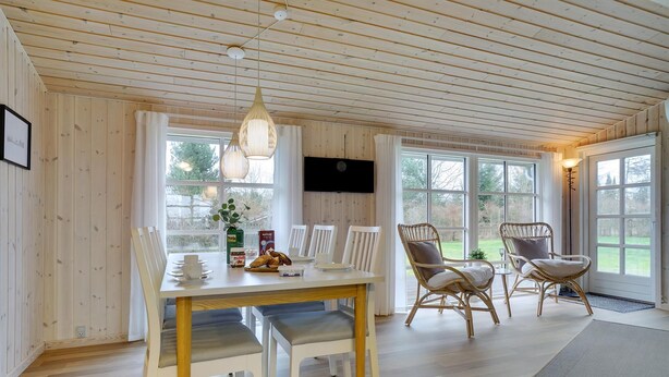 A wooden-paneled room with a dining table, chairs, and a television. - Charming holiday home close to water (Sæby)