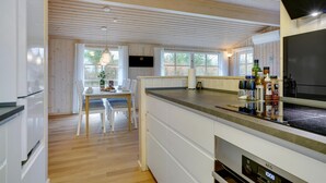 A modern kitchen with wooden ceiling beams, a dining area with a table and chairs, and a large window. - Charming holiday home close to water (Sæby)