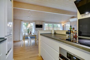 A modern kitchen with wooden ceiling beams, a dining area with a table and chairs, and a large window.