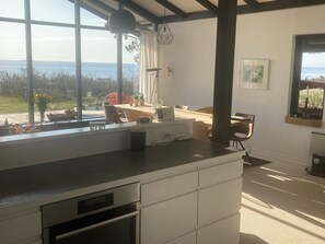 A modern kitchen with a large window, a dining area with a table and chairs, and a view of the sea. - Cozy holiday home on a large beach plot (Martofte)
