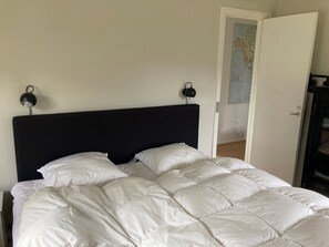 A bed with a black headboard, white bedding, and two black wall-mounted lamps. - Cozy holiday home on a large beach plot (Martofte)