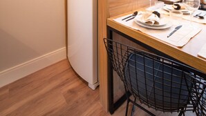 Une cuisine compacte avec un réfrigérateur blanc, des étagères en bois ornées de plantes, une table à manger dressée avec des assiettes, des verres et des couverts.