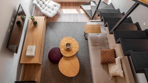 Un appartement moderne de style « loft », doté d’un escalier, d’un canapé, d’un fauteuil rembourré et d’une petite table agrémentée d’objets décoratifs.