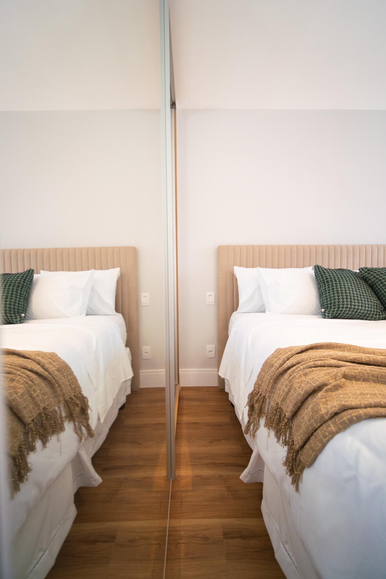 A mirrored room with two beds, each with white bedding and a brown throw blanket.