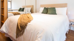 Un lit bien fait, avec du linge de lit blanc et un plaid marron, un grand miroir et un plancher en bois.