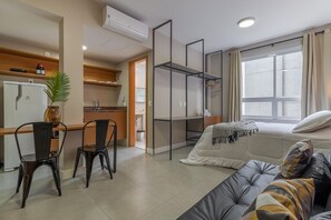 A modern hotel room with a bed, a sofa, a desk with chairs, a kitchenette, and a large window. - Av0811 Studio Avanhandava (São Paulo)