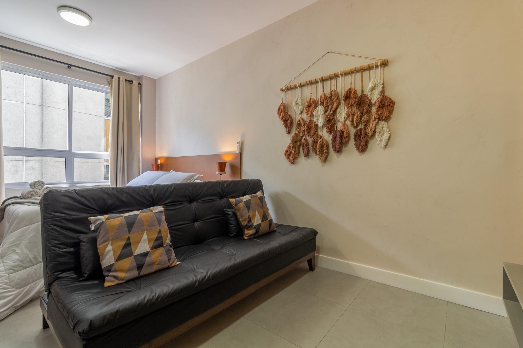 A modern living room with a black leather sofa, a wall-mounted decorative piece, and a large window with curtains.