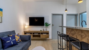 A modern living room with a grey sofa, a coffee table, and a TV mounted on the wall. There is a wooden cabinet with a plant on top and a kitchen area with a bar counter and stools. - Leo166-4 in S o Paulo (São Paulo)