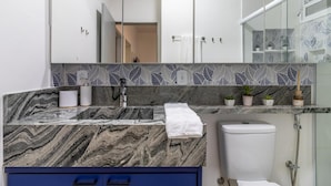 A bathroom with a marble countertop, a white toilet, a glass shower enclosure, and a decorative leaf-patterned backsplash. - Leo166-4 in S o Paulo (São Paulo)