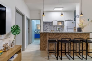 Una cucina moderna con mobili bianchi, una schiena a mosaico in marmo e un'isola centrale con sgabelli da bar.