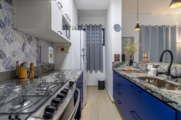 Una cucina moderna con piano cottura a gas, mobili azzurri, un piano di lavoro in marmo e un lavello.