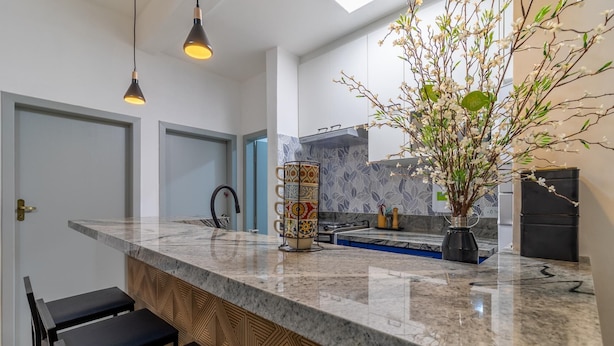 A modern kitchen with a marble countertop, black bar stools, a vase with flowers, and pendant lighting. - Leo166-4 in S o Paulo (São Paulo)