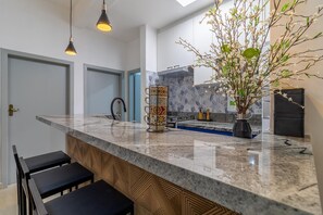 A modern kitchen with a marble countertop, black bar stools, a vase with flowers, and pendant lighting. - Leo166-4 in S o Paulo (São Paulo)