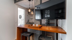 Eine moderne Küche mit Holzauslauf, zwei Barhocker, einem großen Flachbildfernseher an der Wand und Pendelleuchten.