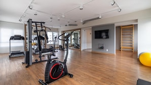 Ein geräumiger Fitnessraum mit verschiedenen Trainingsgeräten, darunter Laufbänder und Kraftgeräte, und einem Holzboden.