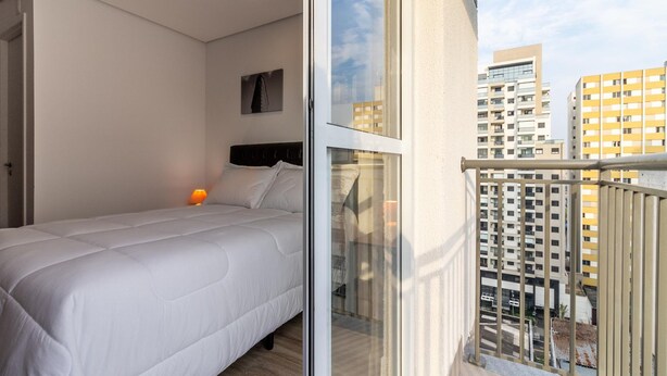 Ein modernes Schlafzimmer mit einem Bett, einem Nachttisch und einem Fenster mit Blick auf eine Stadtlandschaft.
